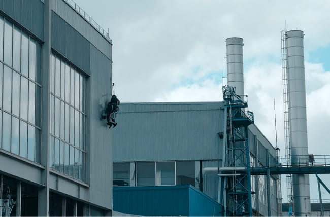 Ein Fensterputzer steigt an einer Leiter an einem Industriegebäude hinauf, um die Fenster zu putzen